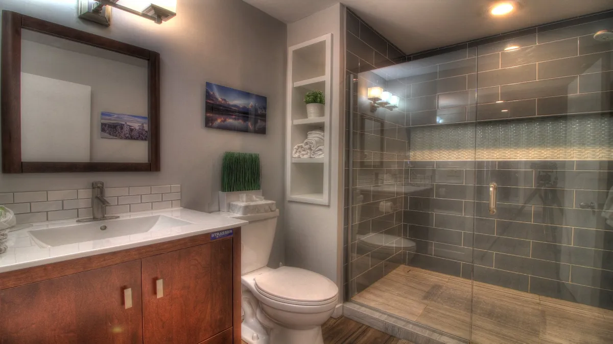 A modern, spa-inspired bathroom with a glass shower stall, sleek vanity with a large mirror, and thoughtful touches like towels and plants on open shelving. Clean lines and natural light create a fresh, rejuvenating vibe.