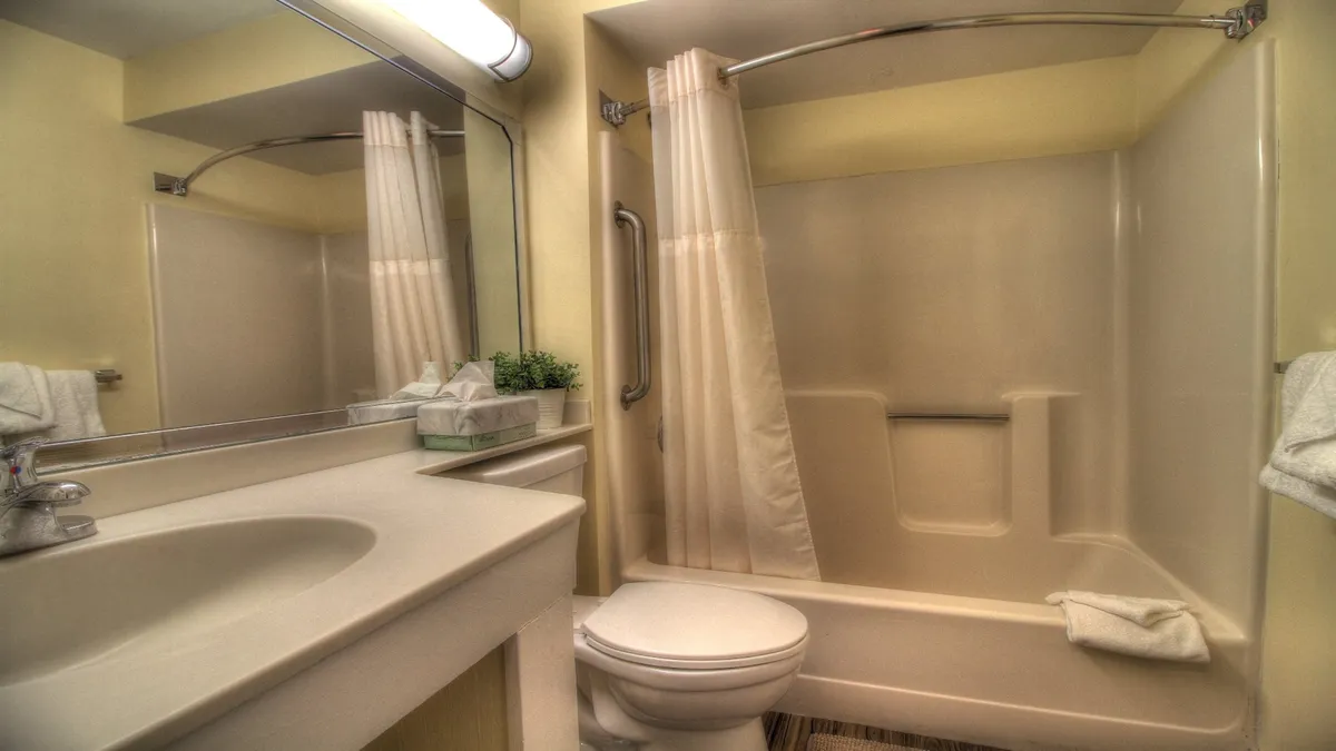 A contemporary bathroom featuring a vanity sink, toilet, glass-enclosed shower area, and a large mirror. The calming color palette and tidy layout underscore an atmosphere of relaxation and privacy.