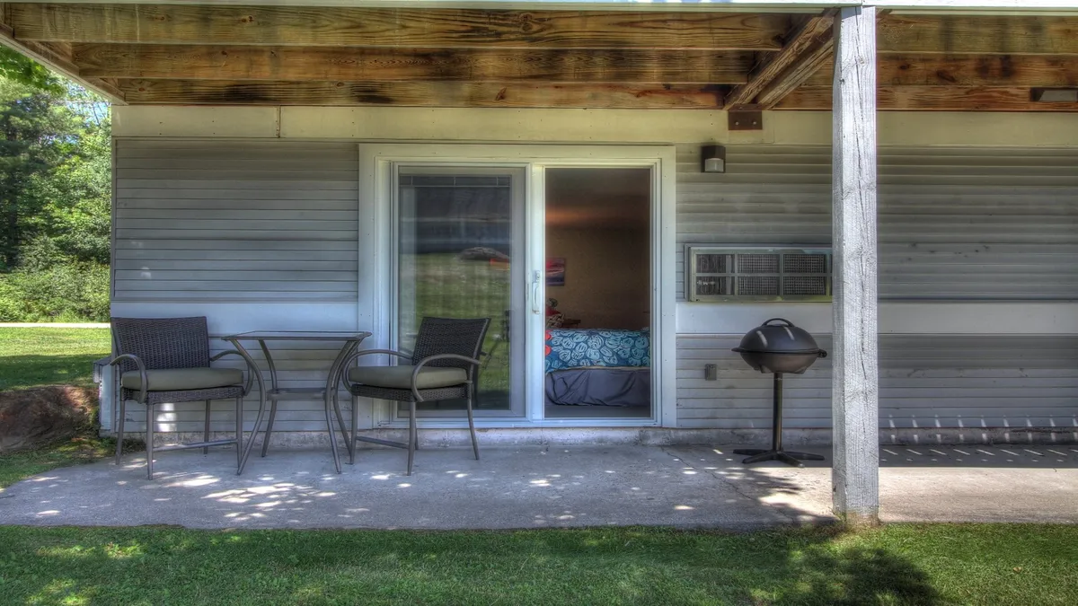 A cozy patio seating area featuring comfortable chairs and a table, adjacent to a sliding glass door, with an electric grill visible. The space is set up for outdoor relaxation or dining, with the grill inviting thoughts of evening barbecues and the seating positioned for socializing or enjoying a morning coffee.