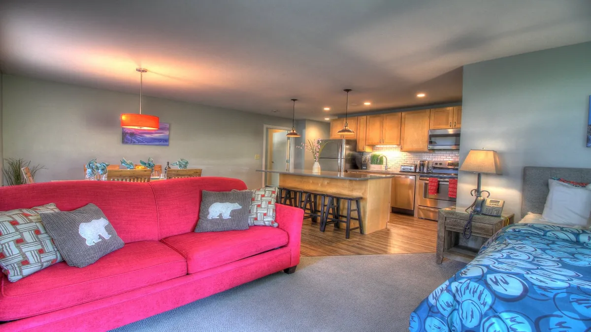 The hero image showcases a welcoming, open-concept living space featuring a vibrant red couch, a spacious kitchen island, and a cozy dining area. The warm lighting and inviting layout evoke a sense of togetherness, highlighting the perfect setting for cooking, relaxing, and sharing meals with family or friends.