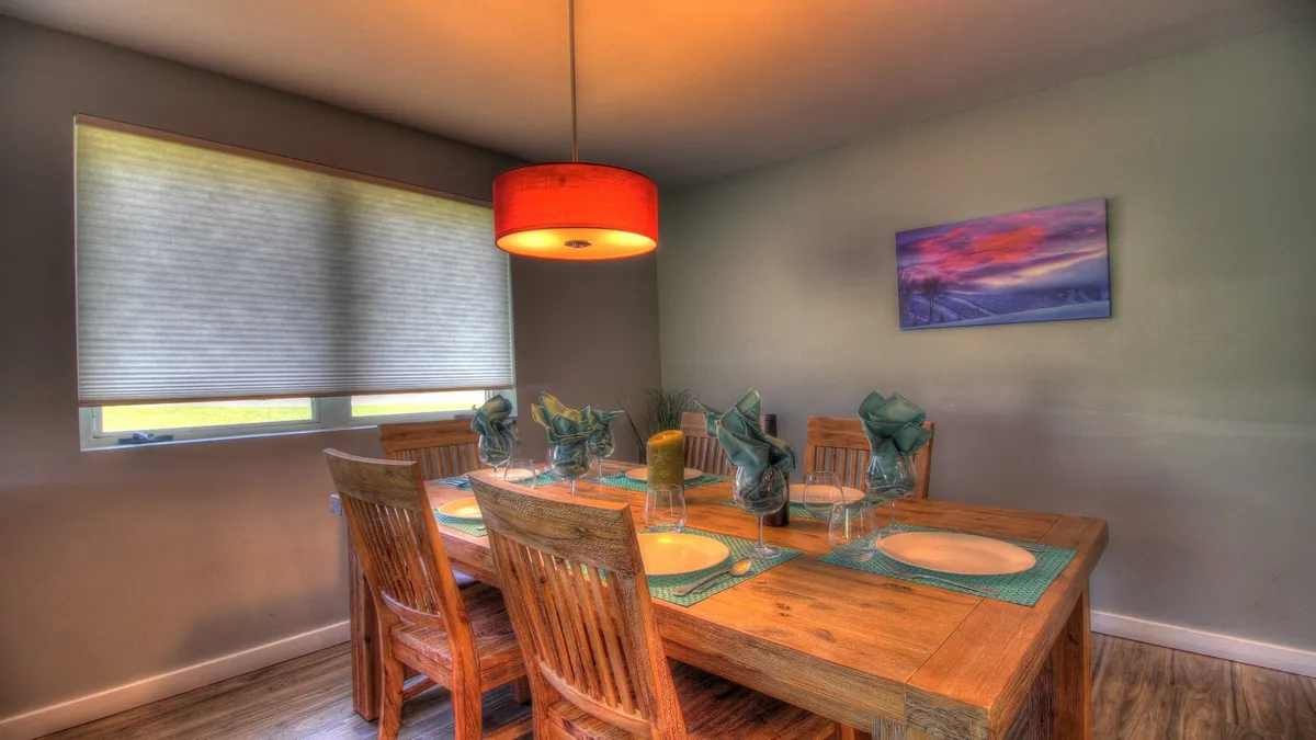 A warmly lit dining area with a dining table set for a meal, a hanging light fixture creating a festive atmosphere, and decorative artwork on the wall. The setting is perfect for shared meals, toasts, and celebrations.