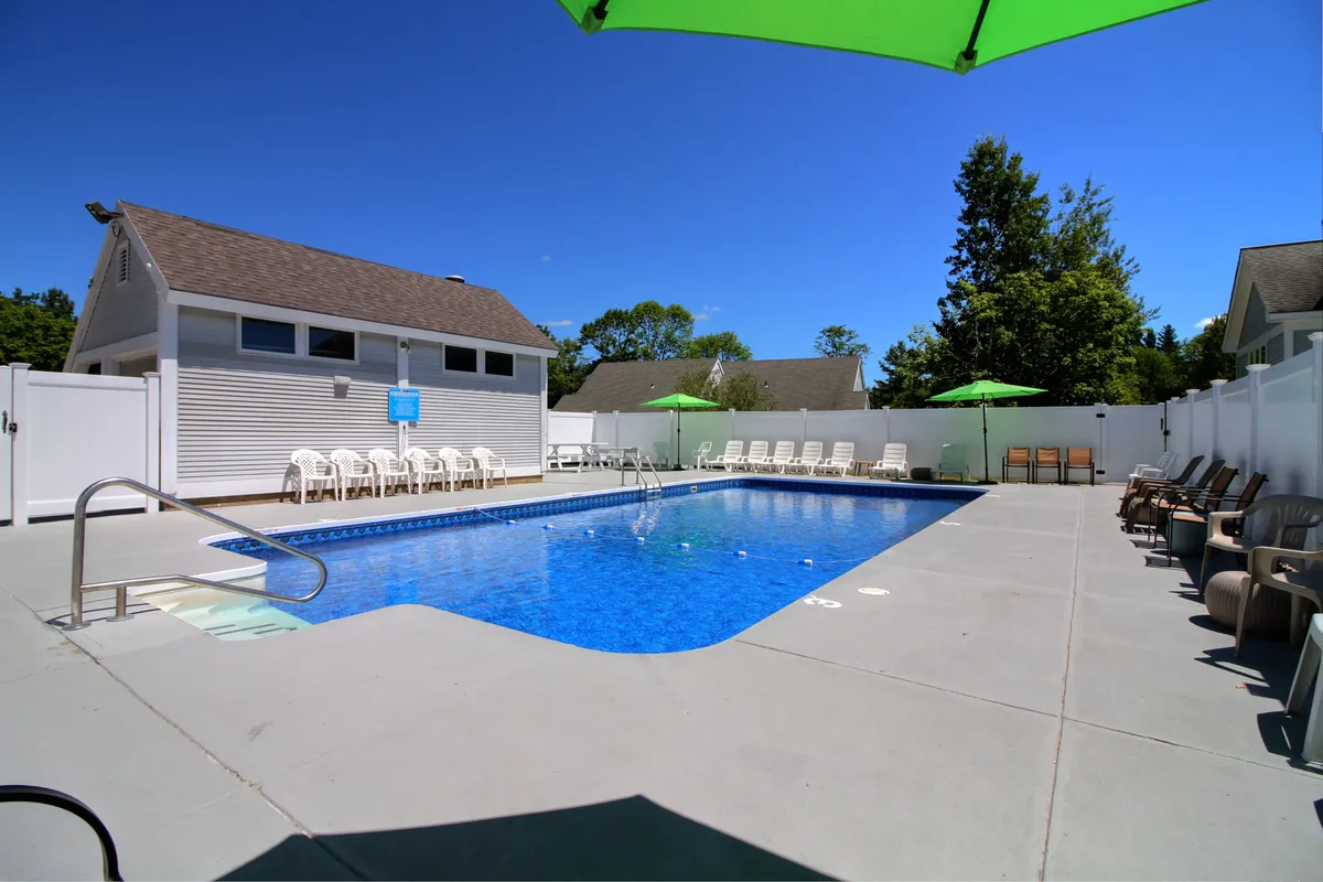 A sparkling swimming pool bordered by green umbrellas, comfortable lounge chairs, and a stylish cabana, offering a lively and social outdoor setting.