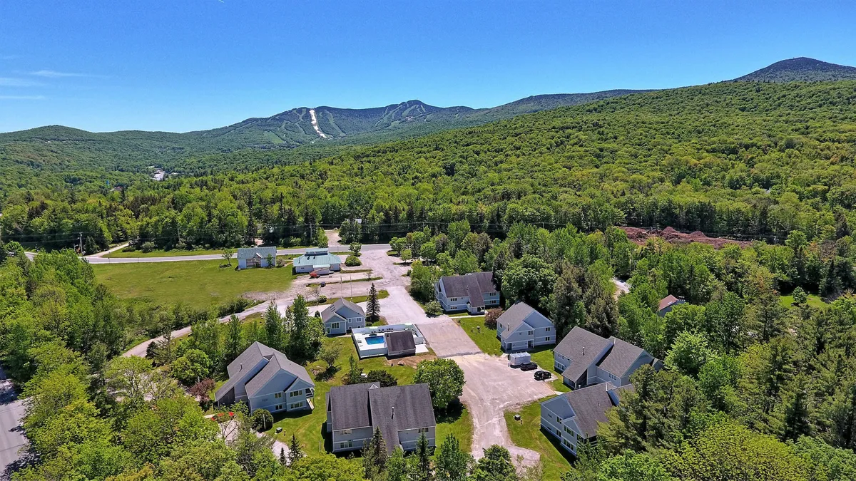 An inviting exterior shot showing residential buildings set against a scenic mountain backdrop, with greenery and a pool area in the foreground. The environment feels lively and outdoors-focused, perfect for group or family gatherings.